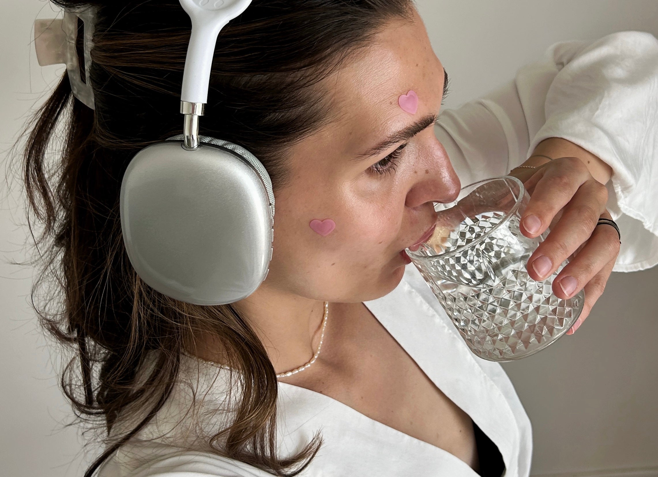 girl with headphones drinking water, wearing heart-shaped microneedle spot patches